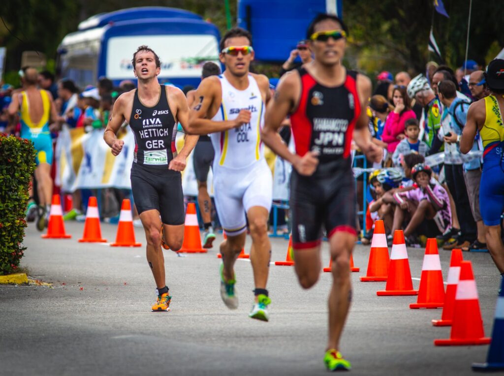 Strong professional male sprinters in sportswear running along racetrack in modern crowded stadium during championship competition