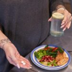 a person holding a jar of liquid over a plate of food